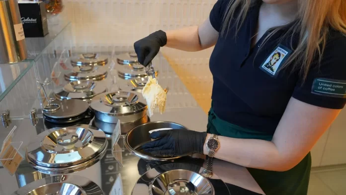 produkcja-lodow-rzemieslniczych-w-maszynie Pracowniczka nabiera lody z metalowych pojemników w profesjonalnej witrynie.